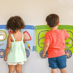 2 kids playing at train activity wall panel