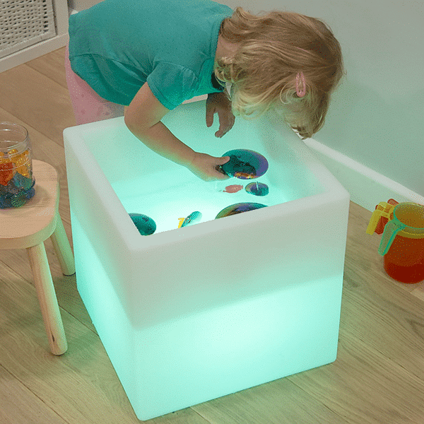 child playing with toys in a sensory table cube lit up green