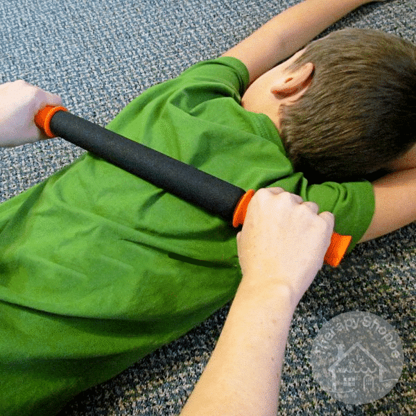 boy laying on the floor, another person using a deep pressure rolling pin on his back